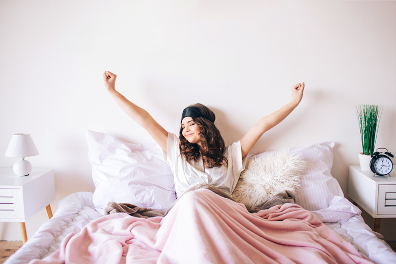 Woman in bed waking up feeling refreshed and energised.